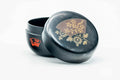 Black-lacquer matcha tea caddy with the lid removed and lying behind, showing the gold floral maki-e on the lid top, three-quarter view