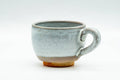 Side profile of the handled cup showing the milky-white glaze above the unglazed lower clay body.