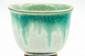 Close-up of a single cup showing green glaze dripping down over the white body