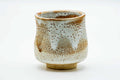 Tall cylindrical Mino-yaki teacup with a creamy white shino glaze blushing to orange, front view.