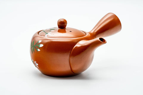 Slightly elevated view showing the painted blossoms across the rounded body and domed lid of the red clay teapot.