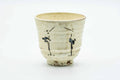 Tall teacup with a milky cream glaze painted with egrets, front view.