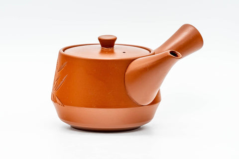 Three-quarter view of the glossy red-orange teapot showing the side handle and bamboo engraving.