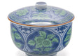 Closeup of the lidded cup showing the hand-painted green-and-blue leaves and red rim line.