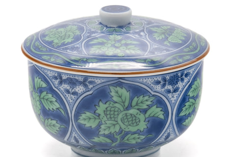 Closeup of the lidded cup showing the hand-painted green-and-blue leaves and red rim line.
