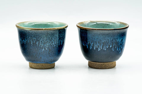 The matching pair of blue drip-glazed cups, front view showing turquoise glaze running over the dark body.