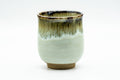 White-and-beige yunomi teacup with a brown hare's-fur drip glaze running down from the rim, front view.