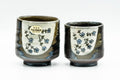 Pair of meoto (his-and-hers) yunomi teacups, a larger and smaller cup glazed white and hand-painted with green floral sprays and calligraphy.