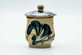 Beige Karatsu-yaki lidded yunomi teacup with blue-green brushed floral decoration, lid on, front view.