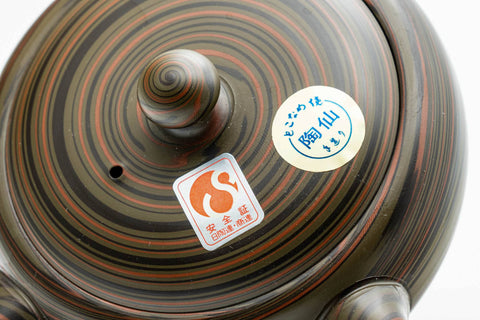 Closeup of the lid knob and swirl detail of the dark green nerikomi kyusu, with a small maker's sticker