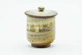 Lidded teacup with a beige drip glaze and spiraling ridges, lid on, front view.