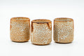 The cylindrical yunomi viewed from rotated front angles, highlighting the mottled Shino glaze.