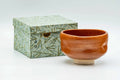 Glossy aka-raku red-glazed matcha chawan shown beside its decorative storage box