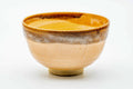 Front view of the Karatsu chawan showing the cream-peach glaze, green grass motif and a dark glazed rim.