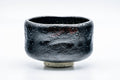 Three-quarter front view of the matte black raku bowl with its rough textured glaze