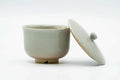 The cup with its lid lifted and propped to one side, tilted to show the glazed interior.