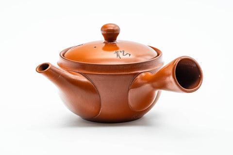 Side profile of the red clay teapot, spout to the left and hollow side handle facing the viewer.