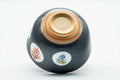 Underside of the grey chawan tilted to reveal the unglazed foot ring and base, with roundel decoration on the body.