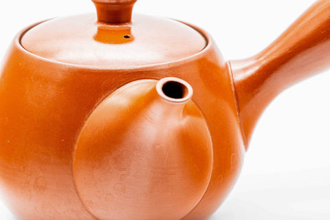 Three-quarter view of the red shudei Tokoname kyusu with lid on, showing the glossy orange clay