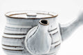 Close-up of the spout and knobbed lid against the white ribbed body.