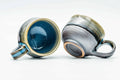 The pair with one cup tipped to show the blue glazed interior and handle.