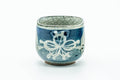 Blue-green glazed yunomi with white floral and geometric motifs, front view.