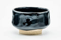Glossy jet-black hand-formed hantsutsu-gata matcha chawan with an exposed clay foot, three-quarter view