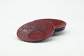 Stack of four red lacquer chataku tea saucers, three-quarter view showing the carved floral and scaled surface.