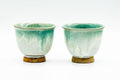 Pair of green drip-glazed Agano-yaki yunomi side by side, front view, green running over a creamy white base above unglazed feet