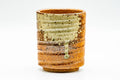 Ash-glazed spiraling Shigaraki-yaki yunomi teacup, front view, orange-tan ridged body with greenish ash-glaze drips, on white background