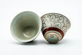 A pair of Kutani-yaki yunomi with a swirling red-and-gold vine pattern, one tipped to show the interior.