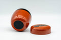 Japanese Natsume - Orange Gold Floral Lacquered Matcha Tea Caddy - 100ml - low-angle view of the closed caddy tilted on its side beside the lid