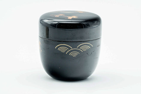 Black-lacquer matcha tea caddy, lid on, front view of the gold soaring-bird and wave maki-e