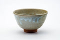 Karatsu-yaki matcha chawan with a mottled beige glaze and red clay foot, three-quarter view.