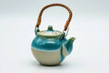 Turquoise drip-glazed Agano-yaki top-handled teapot with a rattan-wrapped handle, three-quarter view over a cream body with the spout to the left