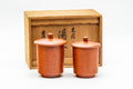 Pair of red shudei Tokoname-yaki lidded yunomi teacups, lids on, shown beside their wooden presentation box.