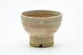 Front view of a footed Hagi-yaki yunomi teacup with a weathered beige glaze and peach gohonte spots, raised on a tall foot.