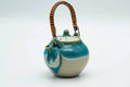 Turquoise Agano-yaki top-handled teapot, front view with the rattan handle raised and turquoise glaze dripping down the cream body
