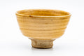 Slight three-quarter view of the Ki-Seto chawan, emphasising its tall foot and amber-yellow glaze.