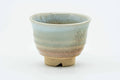 Small flared Hagi-yaki teacup with a weathered beige, pink, and white glaze, front view.