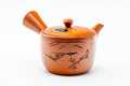 Three-quarter front view of a red shudei Tokoname-yaki kyusu engraved with a mountainous landscape, lid on, side handle right and spout left.