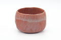 Front view of the raku bowl showing its irregular lip and warm red glaze blushed with grey.