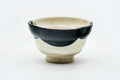 Small cup with a cream glaze painted with a black-brushwork Okame (smiling woman) face, front view.