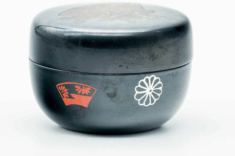 Black-lacquer floral matcha tea caddy, close view with lid on, centered on the red crest on the body