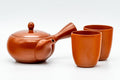 Red shudei Tokoname-yaki tea set, three-quarter view of the side-handle kyusu teapot beside one yunomi teacup.