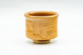 Three-quarter view of the amber-glazed guinomi showing the mottled glaze and form.