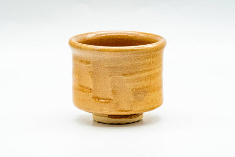 Three-quarter view of the amber-glazed guinomi showing the mottled glaze and form.