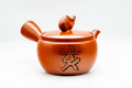 Red shudei Tokoname-yaki kyusu teapot, three-quarter front view, with a small pig figurine perched as the lid knob.