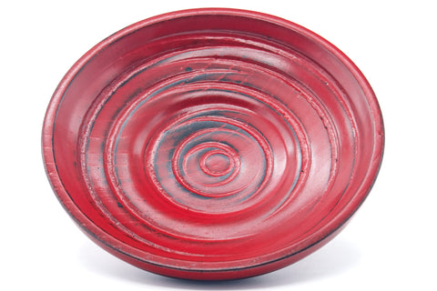 Close-up of a single red wooden chataku saucer, showing the turned concentric spiral rings and red finish
