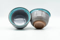 Two blue turquoise drip-glazed teacups at an angle, one tilted to reveal the glazed interior